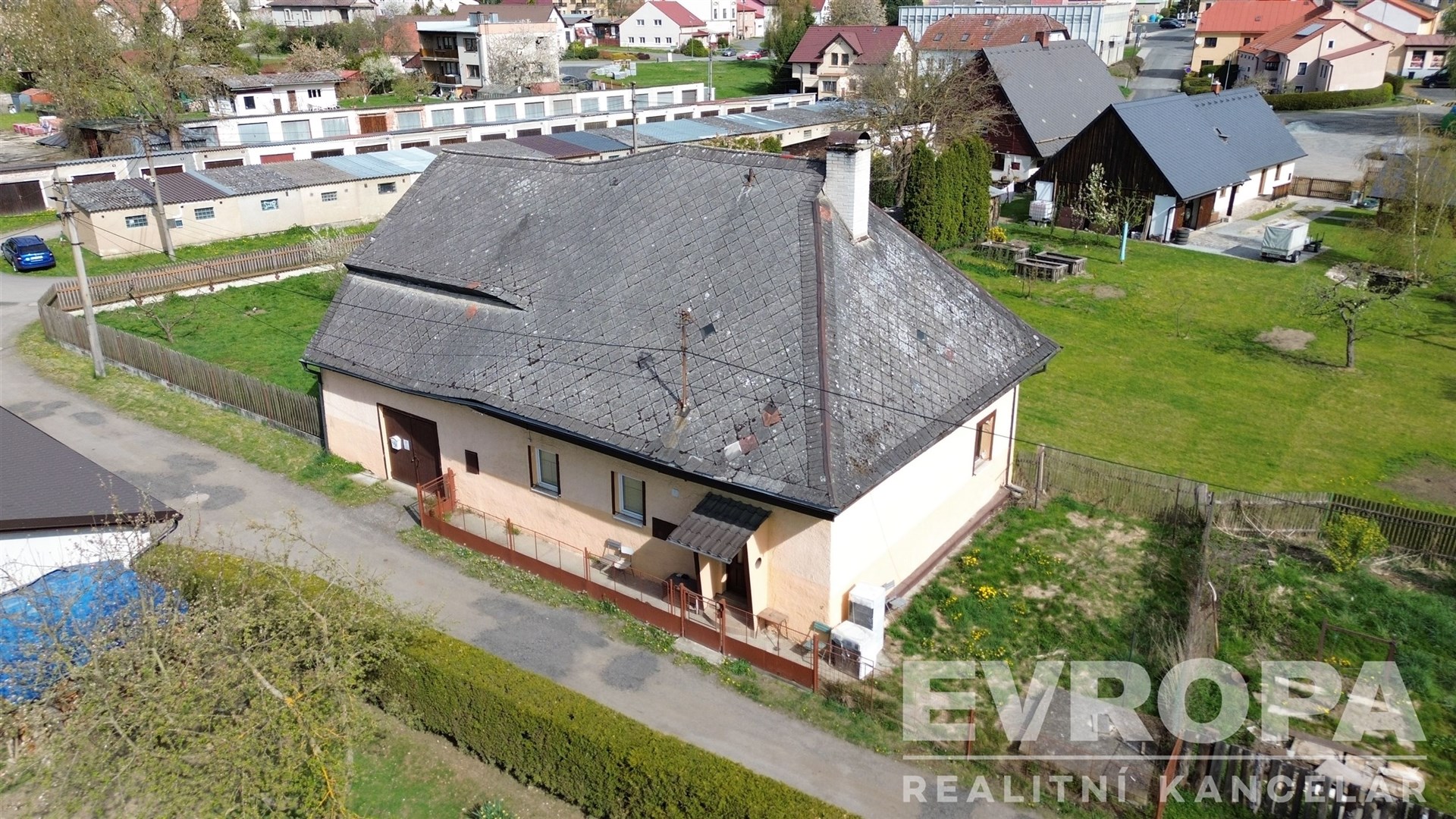Starší rodinný dům s šikmou střechou, omítkou a zahradou v poklidném venkovském prostředí.
