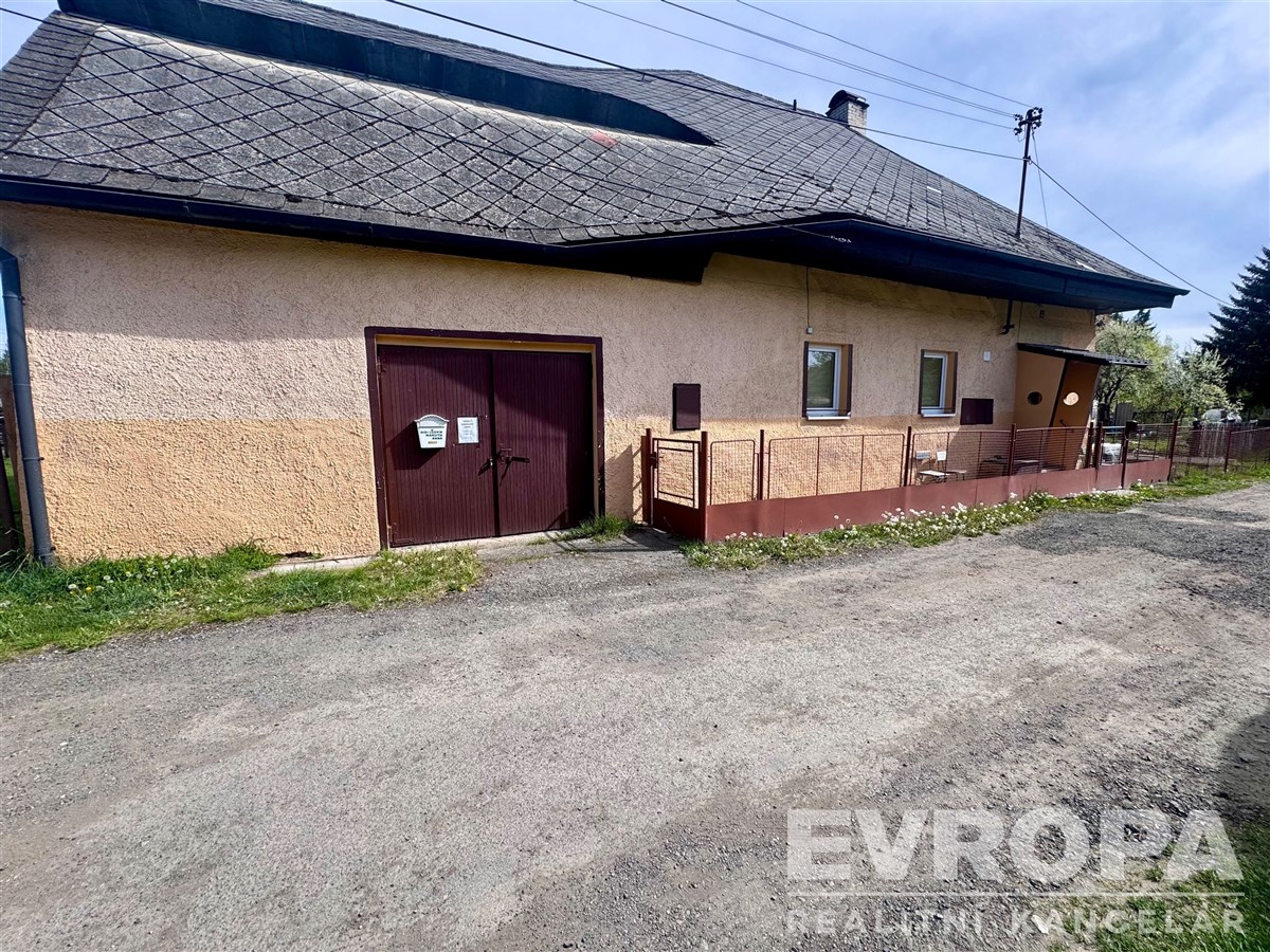 Exteriér rodinného domu s garáží, omítková fasáda, střecha s eternitovými šablonami, klidná venkovská lokalita, prostorná příjezdová cesta.
