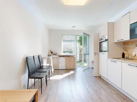 Světlá kuchyň s vinylovou podlahou, moderními spotřebiči a výhledem do zahrady, nabízí vestavěné skříně a elegantní design. | Prodej bytu, 1+1, 36 m²