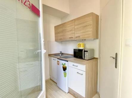 kuchyně s světle hnědé skříně, myčka, deformace, dřevěná podlaha, a mikrovlnná trouba | Pronájem bytu, 1+1, 21 m²