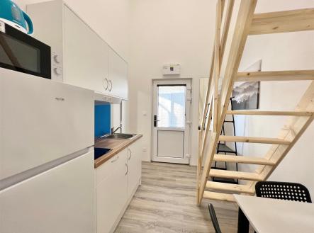 Malá kuchyň s moderními spotřebiči, dřevěným schodištěm a světlou vinylovou podlahou, ideální pro kompaktní bydlení. | Pronájem bytu, 2+1, 35 m²