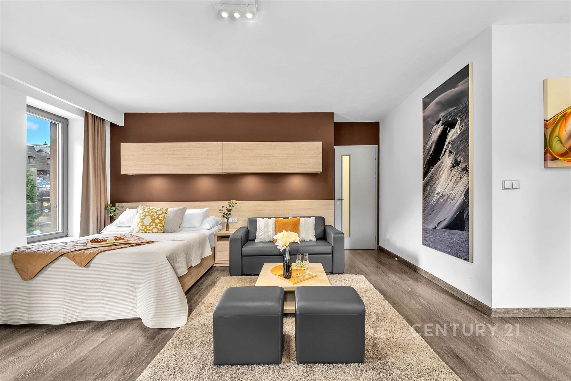 Světlý obývací pokoj s parketovou podlahou, moderní design, velká okna nabízí přirozené světlo a otevřený prostor s pohodlným sezením.