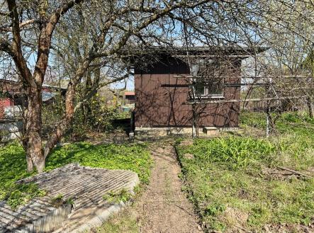 Malá zahradní chatka s dřevěnou fasádou uprostřed klidné zahrady. Okolní zelené stromy poskytují přirozený stín a soukromí. | Prodej - pozemek, zahrada, 266 m²