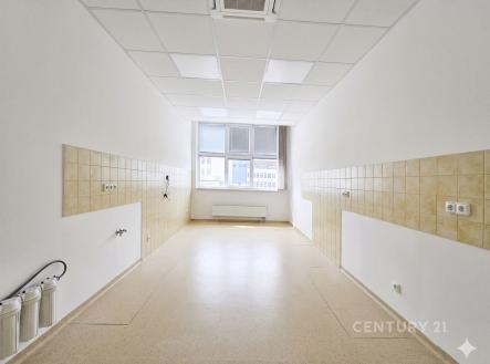 Prázdná kuchyně s dlažbou, připravená k rekonstrukci, disponuje velkými okny a bílými stěnami, ideální pro moderní úpravy. | Pronájem - jiné, 18 m²