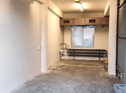 Úzká garáž se surovou betonovou podlahou, plechová vrata, bílými stěnami a stropním osvětlením, ideální pro parkování menšího auta. | Pronájem - skladovací prostor, 33 m²