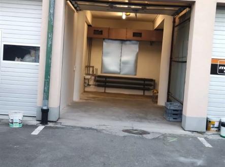 Průmyslová garáž s betonovou podlahou, vysokým stropem a rozměrnými vraty, ideální pro skladování nebo parkování větších vozidel. | Pronájem - skladovací prostor, 33 m²