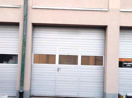 Prázdný prostor s garážovými vraty, betonová podlaha, vhodný pro skladování nebo parkování, dobrý stav, snadný přístup. | Pronájem - skladovací prostor, 33 m²