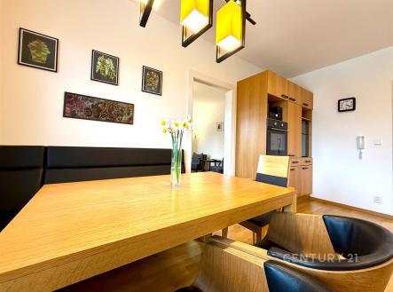 Jídelna s dřevěným stolem a parketovou podlahou, moderní vestavěné skříně a světlé osvětlení, elegantní designový styl. | Prodej - dům/vila, 124 m²