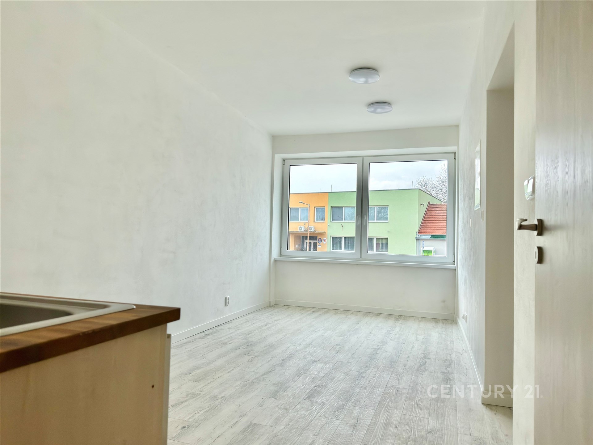 Světlý obývací pokoj s velkými okny, laminátovou podlahou a moderním designem, ideální pro útulné bydlení v rekonstruovaném bytě.
