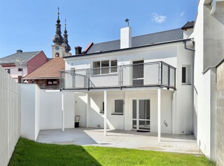 Přízemí domu s moderní fasádou, prostornou terasou a upraveným dvorkem. Dům má velká okna a nachází se ve zrekonstruované oblasti blízko kostela. | Prodej - dům/vila, 118 m²