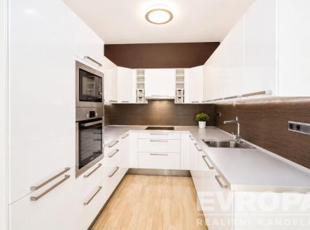 Moderní kuchyň s bílými skříňkami, vestavěnými spotřebiči a parketovou podlahou. Světlý prostor s moderním osvětlením a elegantním designem. | Pronájem bytu, 2+kk, 53 m²