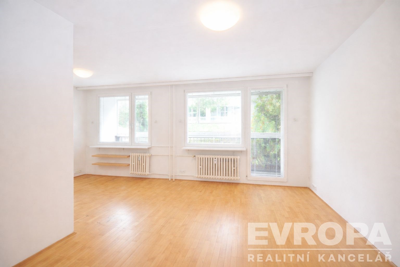 Světlý obývací pokoj s parketovou podlahou, velkými okny a moderním designem nabízí prostorné a vzdušné prostředí pro pohodlné bydlení.