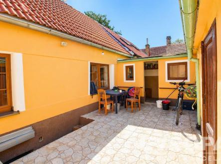 Prostorný dvorek s dlažbou, venkovním nábytkem a žlutou fasádou nabízí příjemné venkovní posezení. | Prodej - dům/vila, 45 m²