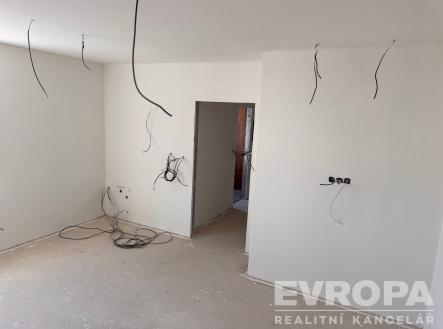 Prázdná místnost s nedokončenou betonovou podlahou a bílými zdmi, příprava na elektroinstalaci, moderní rekonstrukce, čistý design | Prodej bytu, 1+kk, 27 m²