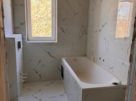 Moderní koupelna s mramorovými obklady, vanou a velkým oknem poskytujícím přirozené světlo, v rekonstruovaném stavu. | Prodej bytu, 1+kk, 27 m²