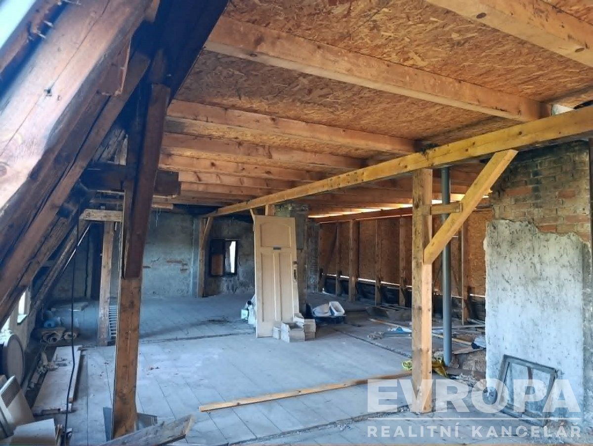 Podkrovní prostor s dřevěnými trámy, původní stěny a dřevěná podlaha, ideální pro rekonstrukci a vytvoření světlého moderního interiéru.