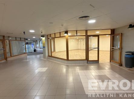 Prázdný obchodní prostor s dlažbou na podlaze, velkými prosklenými stěnami a moderním osvětlením, ideální pro komerční využití. | Pronájem - obchodní prostor, 132 m²