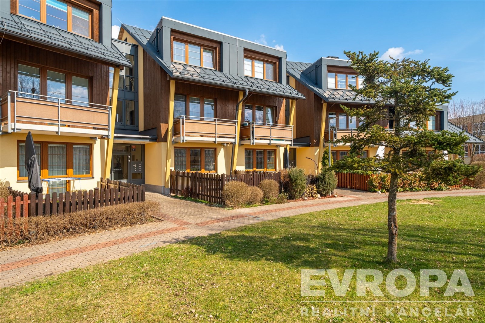 Řadový rodinný dům s dřevěným obkladem, velká okna, upravená zahrada, moderní styl, klidná lokalita.