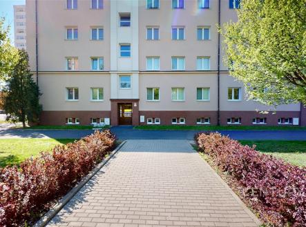 Venkovní fasáda bytového domu se světlou omítkou, upraveným přístupovým chodníkem a okolní zelení, vhodné pro městské bydlení. | Prodej bytu, 3+1, 73 m²