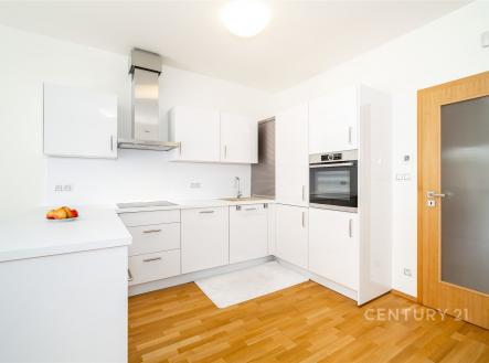 Moderní kuchyň s parketovou podlahou a vestavěnými spotřebiči, v bílém provedení. Světlý, elegantní design s dřevěnými doplňky. | Prodej bytu, 3+kk, 105 m²