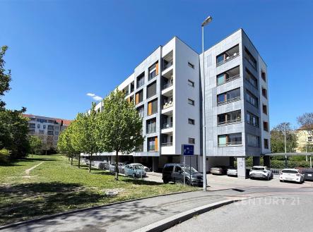 Moderní bytový dům s balkony v klidné lokalitě, fasáda s čistými liniemi, parkoviště vedle budovy, obklopený zelenými plochami a stromy. | Prodej bytu, 3+kk, 105 m²