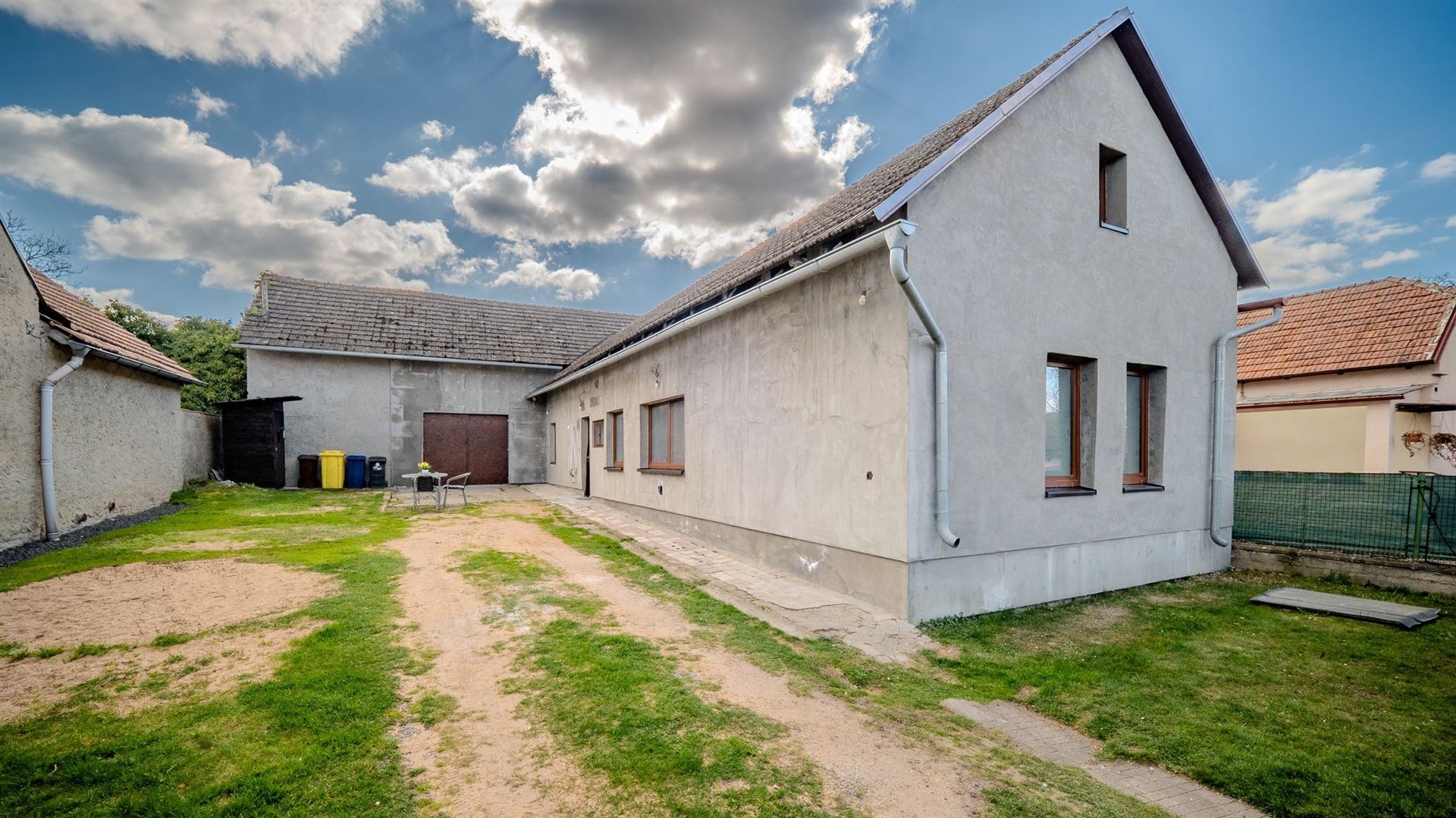 Exteriér rodinného domu s novou fasádou, štěrková příjezdová cesta, prostorný dvůr, vhodné k rekonstrukci, klidná lokalita.