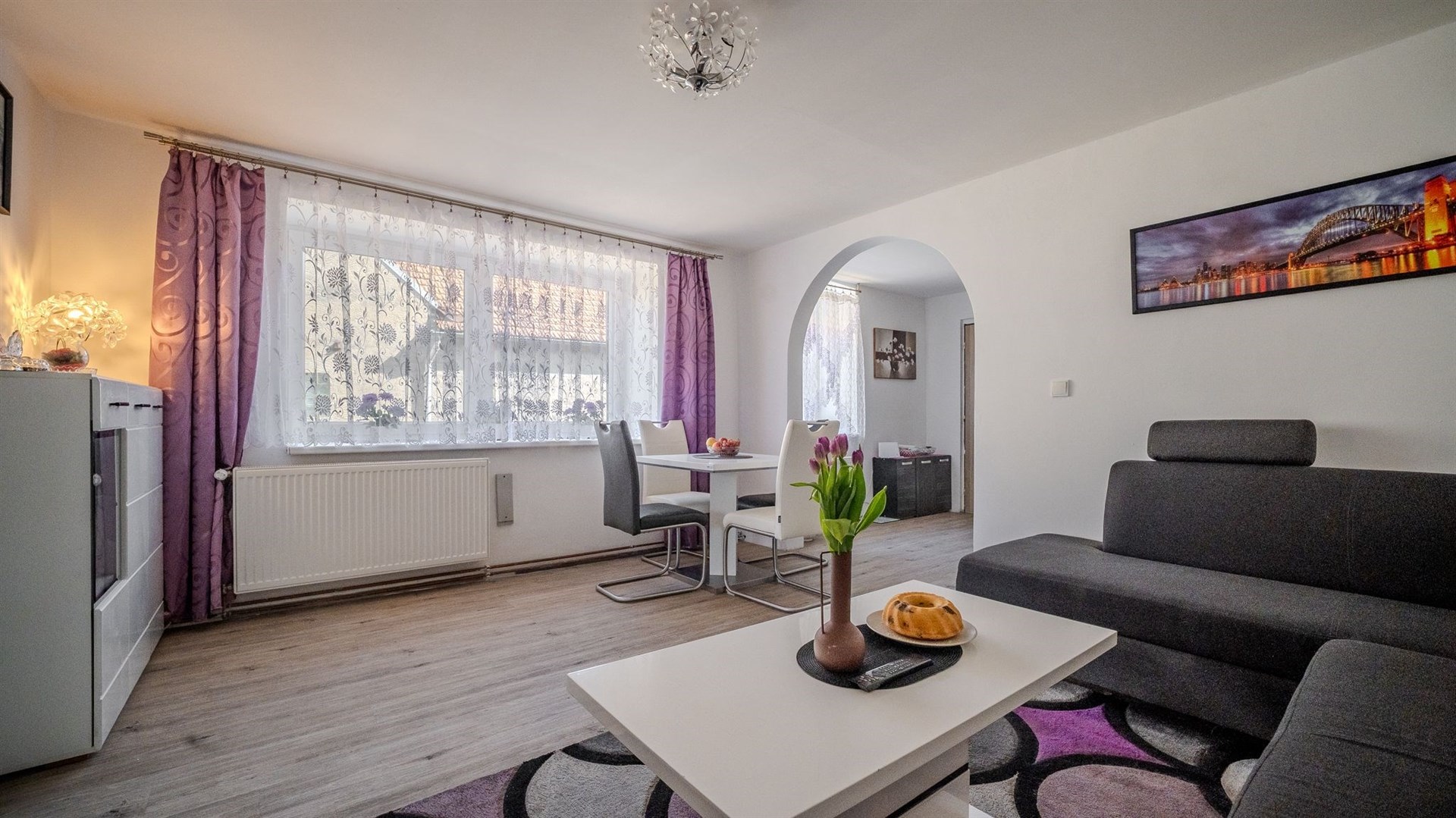 Světlý obývací pokoj s moderní sedací soupravou, parketovou podlahou, velkými okny a elegantním nábytkem v rekonstruovaném bytě.