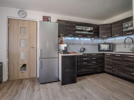 Moderní kuchyň s tmavou dřevěnou linkou, parketovou podlahou a vestavěnými spotřebiči, nabízí světlý a elegantní prostor. | Prodej - dům/vila, 71 m²