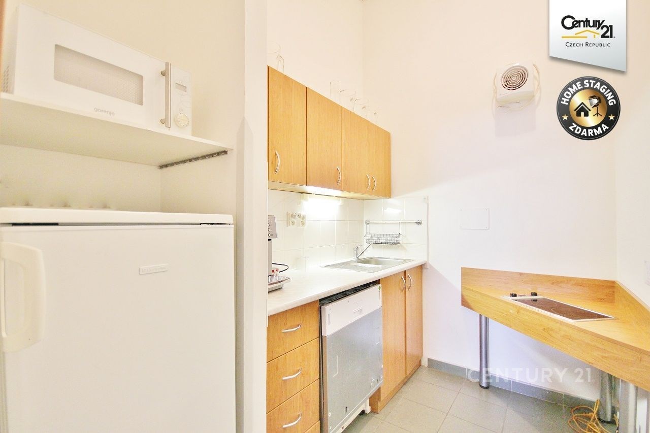 Kompaktní kuchyň s bílou dlažbou, světlými dřevěnými skříňkami a vestavěnými spotřebiči nabízí moderní a funkční prostor pro vaření.