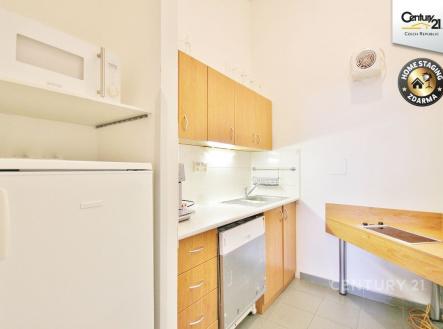 Kompaktní kuchyň s bílou dlažbou, světlými dřevěnými skříňkami a vestavěnými spotřebiči nabízí moderní a funkční prostor pro vaření. | Pronájem - kanceláře, 17 m²