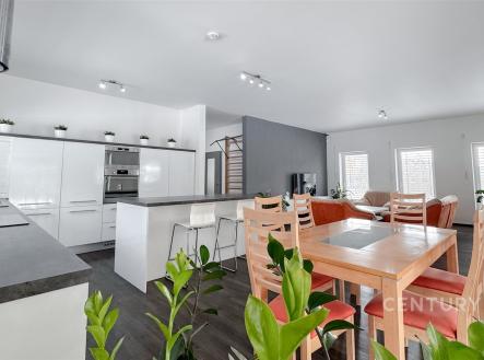 Moderní kuchyň s parketovou podlahou, světlým nábytkem a velkými okny. Propojená s obývacím pokojem a jídelním prostorem, nabízí komfortní bydlení. | Pronájem - dům/vila, 210 m²