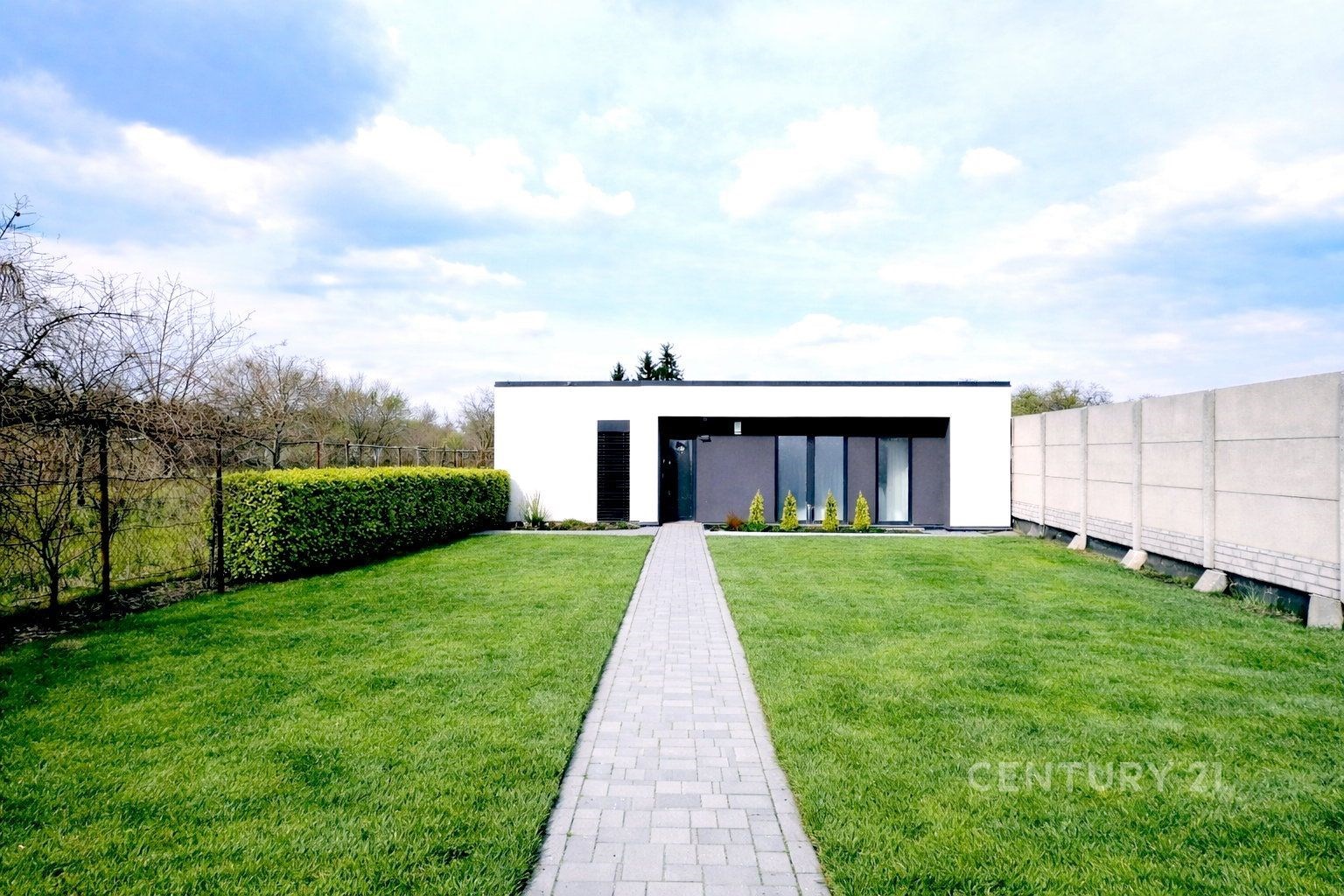 Moderní zahrada s udržovaným trávníkem a dlažebním chodníkem vedoucím k minimalistickému domu, nabízí klidnou lokalitu a soukromí.