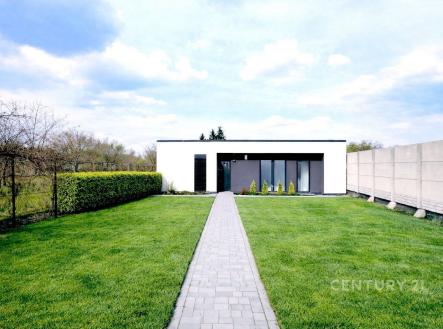 Moderní zahrada s udržovaným trávníkem a dlažebním chodníkem vedoucím k minimalistickému domu, nabízí klidnou lokalitu a soukromí. | Prodej - pozemek pro bydlení, 1 057 m²