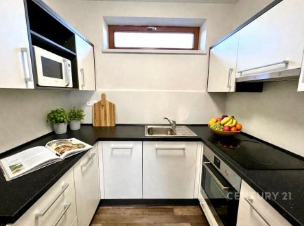 Moderní kuchyň s bílými skříňkami, černou pracovní deskou a vestavěnými spotřebiči, světlý prostor s parketovou podlahou | Pronájem bytu, 2+kk, 48 m²