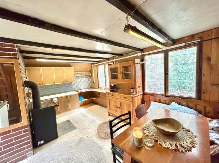 Rustikální kuchyň se dřevěnými obklady, velkými okny a krbovými kamny, nabízí útulný prostor pro vaření a relaxaci. | Prodej - chata/rekreační objekt, 34 m²