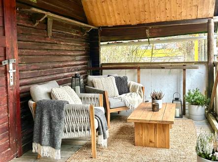 Krytá terasa s dřevěným stropem a stěnami, vybavená pohodlnými křesly a dřevěným stolkem, útulné venkovní posezení, přírodní dekorace. | Prodej - chata/rekreační objekt, 34 m²