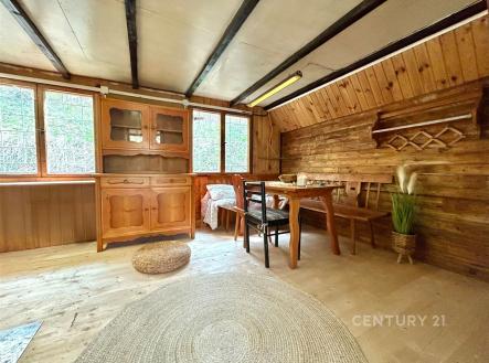 Rustikální obývací pokoj s dřevěným obložením, velkými okny a parketovou podlahou nabízí útulnou atmosféru chaty. | Prodej - chata/rekreační objekt, 34 m²