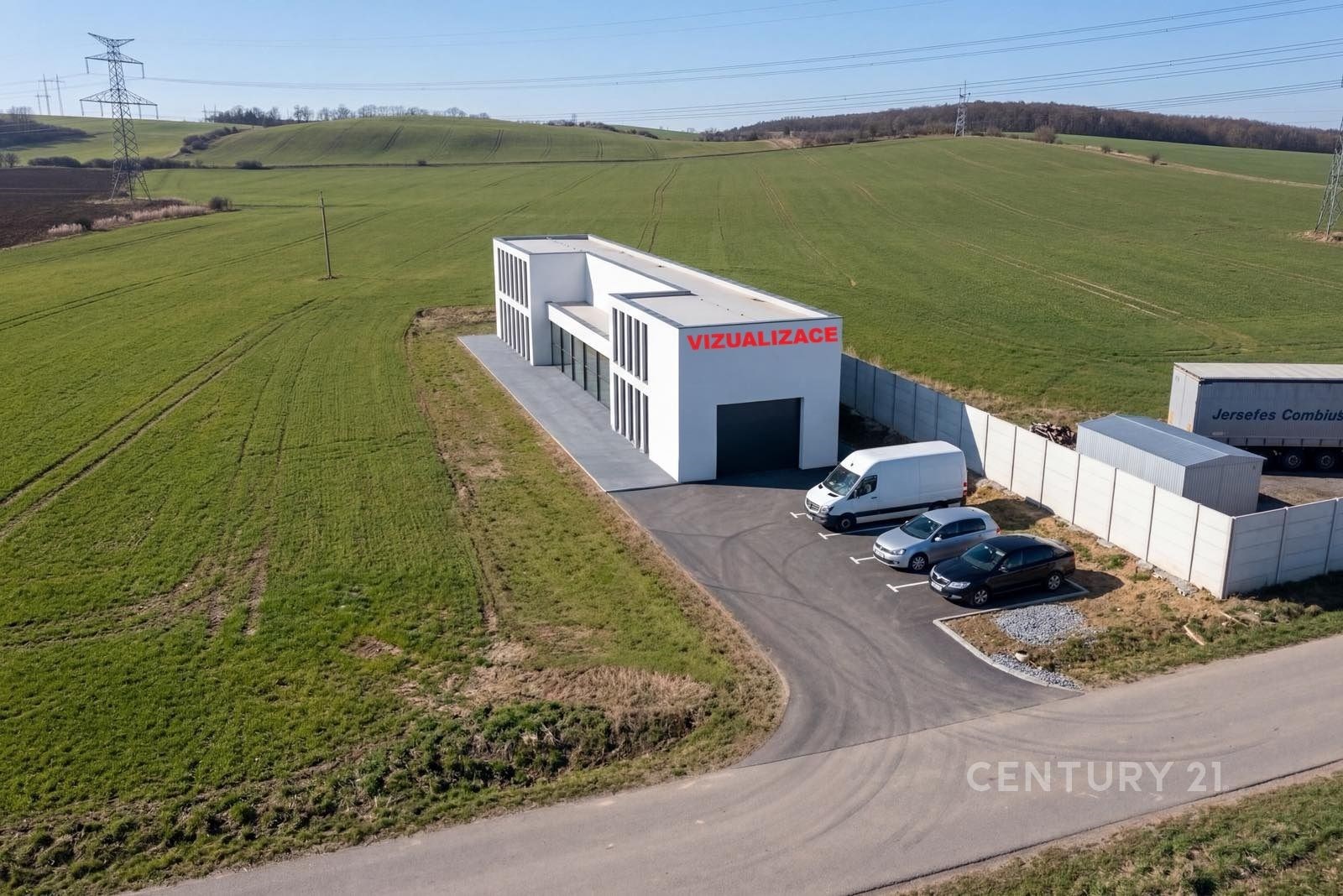 Průmyslová hala s moderním designem, velkým parkovištěm a novou fasádou, obklopená zelení a snadným přístupem po asfaltové cestě.