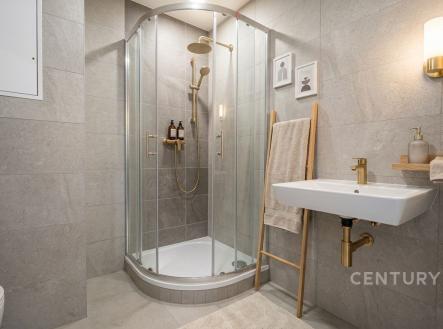 Koupelna s moderní sprchou, dlažbou a zlatými doplňky, laděná v neutrálních tónech, elegantně osvětlená s minimalistickým designem. | Pronájem bytu, 1+kk, 34 m²