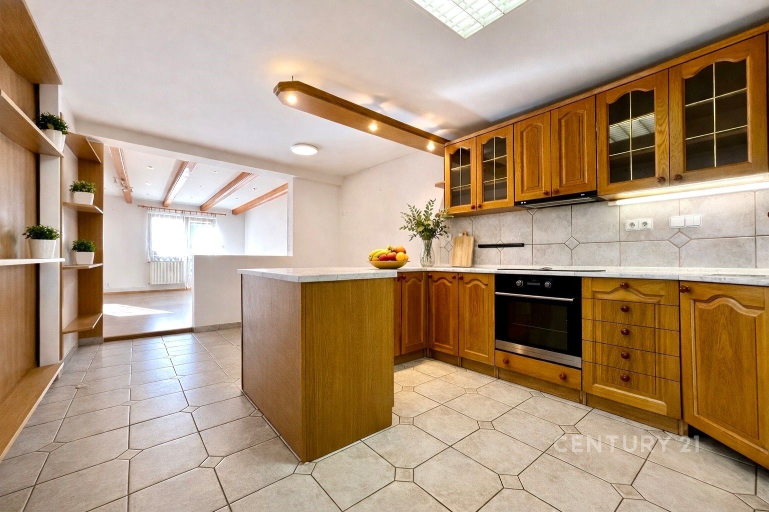 Prostorná kuchyň s dřevěnými skříňkami, dlažbou a vestavěnou troubou. Velká okna v obývacím pokoji zajišťují světlost interiéru.