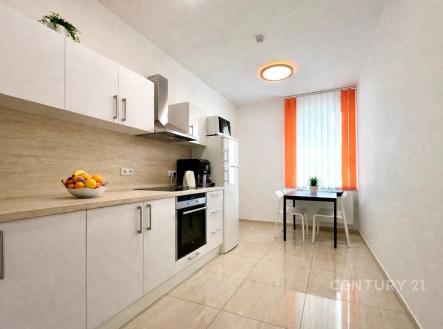 Moderní kuchyň s dlažbou, bílými skříňkami a vestavěnými spotřebiči, která má velká okna s oranžovými závěsy, poskytující dostatek světla. | Pronájem - skladovací prostor, 81 m²