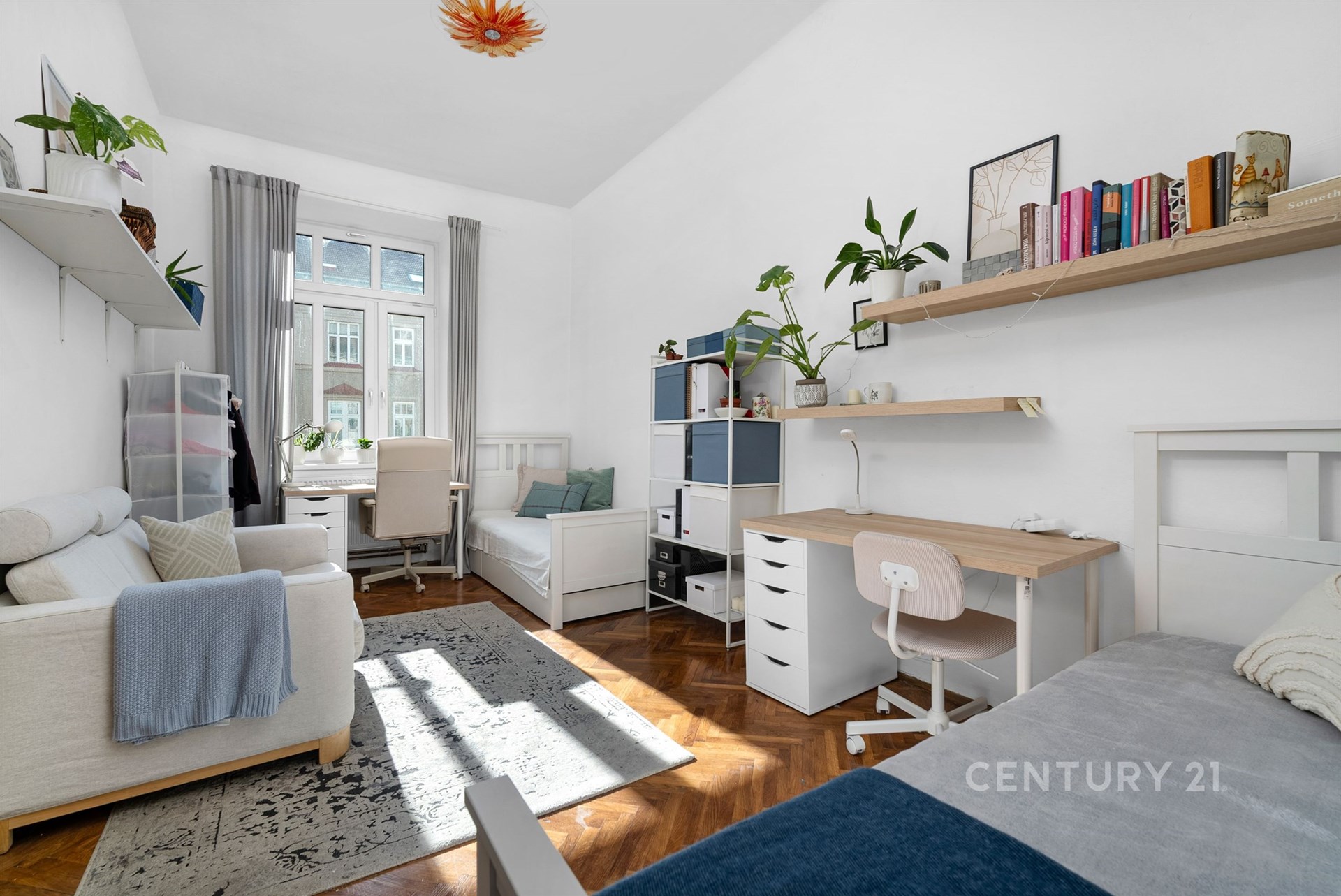 Dětský pokoj s parketovou podlahou, velkými okny a moderním vybavením. Světlý prostor s vestavěnými skříněmi a pracovním stolem.