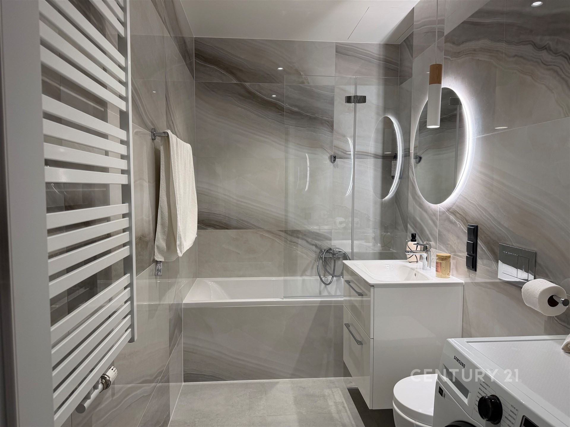 Moderní koupelna s mramorovou dlažbou, vestavěným osvětlením a vanou. Součástí je také stylový umyvadlový set a prostor pro pračku.
