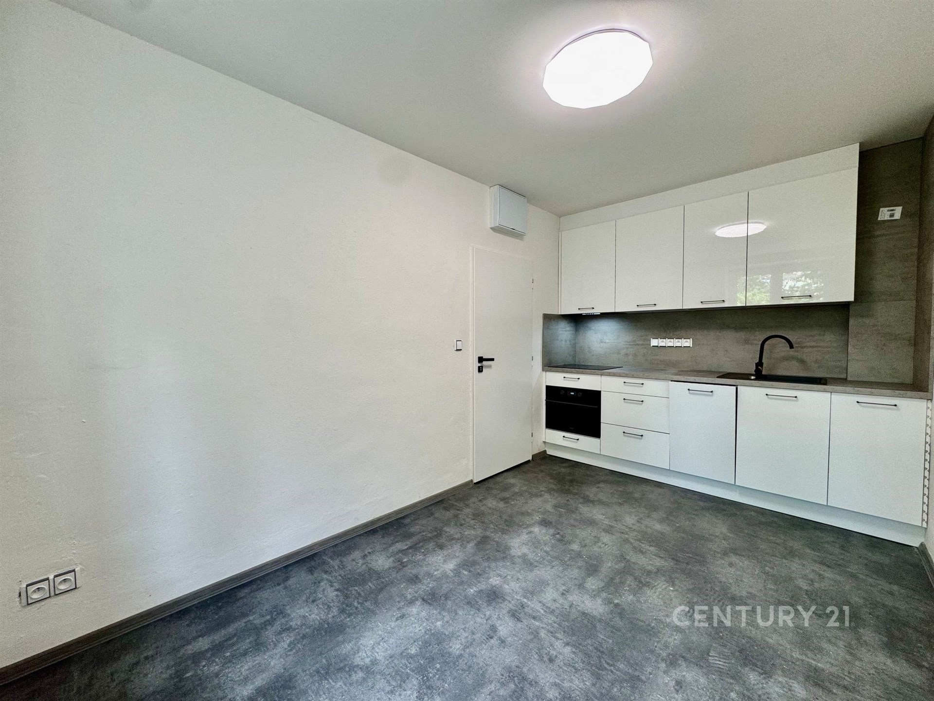 Moderní kuchyň s dlažbou, bílými lesklými skříňkami a vestavěnými spotřebiči. Prostorná a světlá s minimalistickým designem.