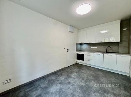 Moderní kuchyň s dlažbou, bílými lesklými skříňkami a vestavěnými spotřebiči. Prostorná a světlá s minimalistickým designem. | Pronájem bytu, 1+1, 48 m²