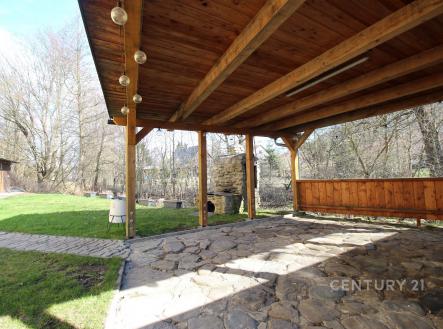 Zastřešená terasa s kamennou dlažbou, dřevěným stropem a výhledem do zahrady. Nabízí prostor pro venkovní posezení a je obklopena zelení. | Prodej - hotel, 350 m²