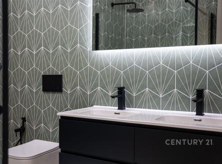 Moderní koupelna s tmavou dlažbou, designové obklady a velké zrcadlo. Elegantní umyvadlo s integrovaným osvětlením a černé doplňky. | Prodej bytu, 4+kk, 104 m²