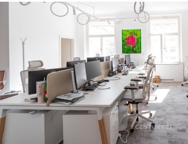 Moderní kancelář s parketovou podlahou, velkými okny a světlým nábytkem, ideální pro produktivní pracovní prostředí.