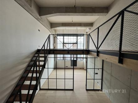 Moderní mezonetový interiér s parketovou podlahou a velkými okny. Přiznané betonové stropy a kovové zábradlí dodávají industriální styl. | Pronájem bytu, 3+kk, 91 m²