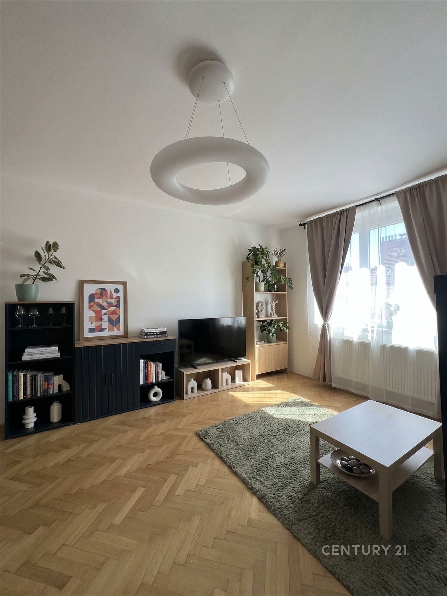 Světlý obývací pokoj s parketovou podlahou.